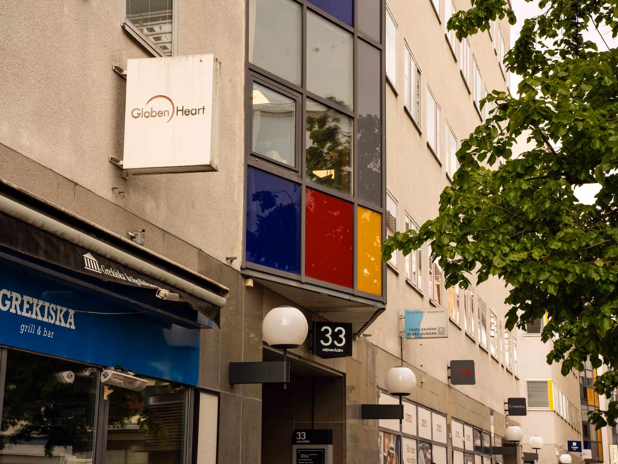 Fasaden på en byggnad med skyltar för Globen Heart och Grekiska grill & bar vid Arenavägen 33.