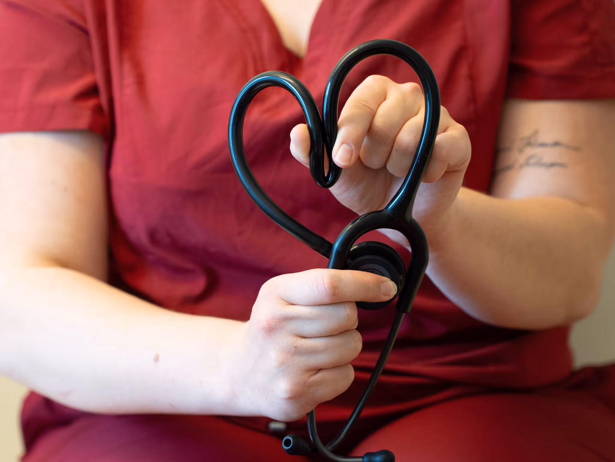 Person in red scrubs holding a black stethoscope shaped like a heart.